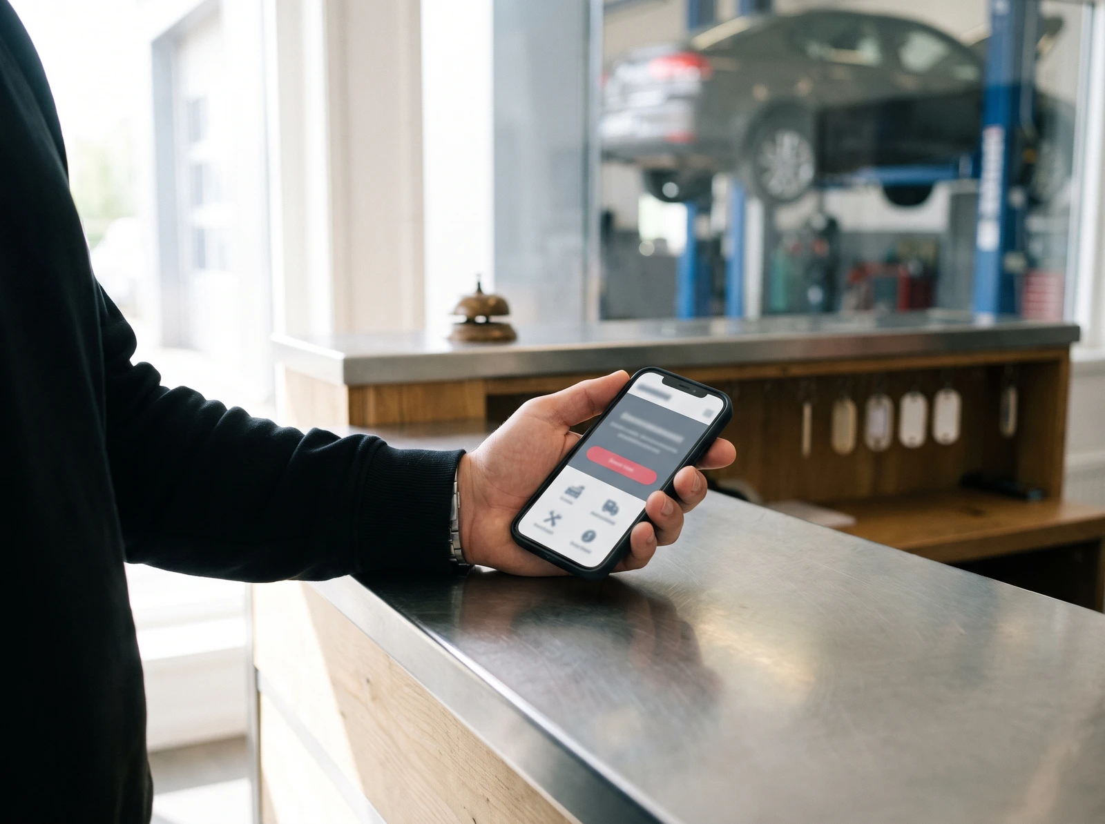 Customer holding a phone showing a garage website booking request screen at the reception counter